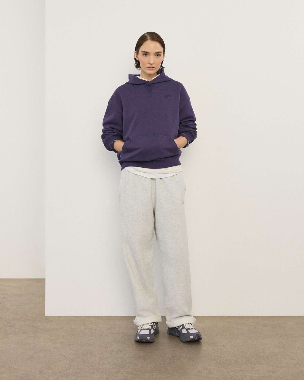A woman wearing New Balance standing in front a white wall.