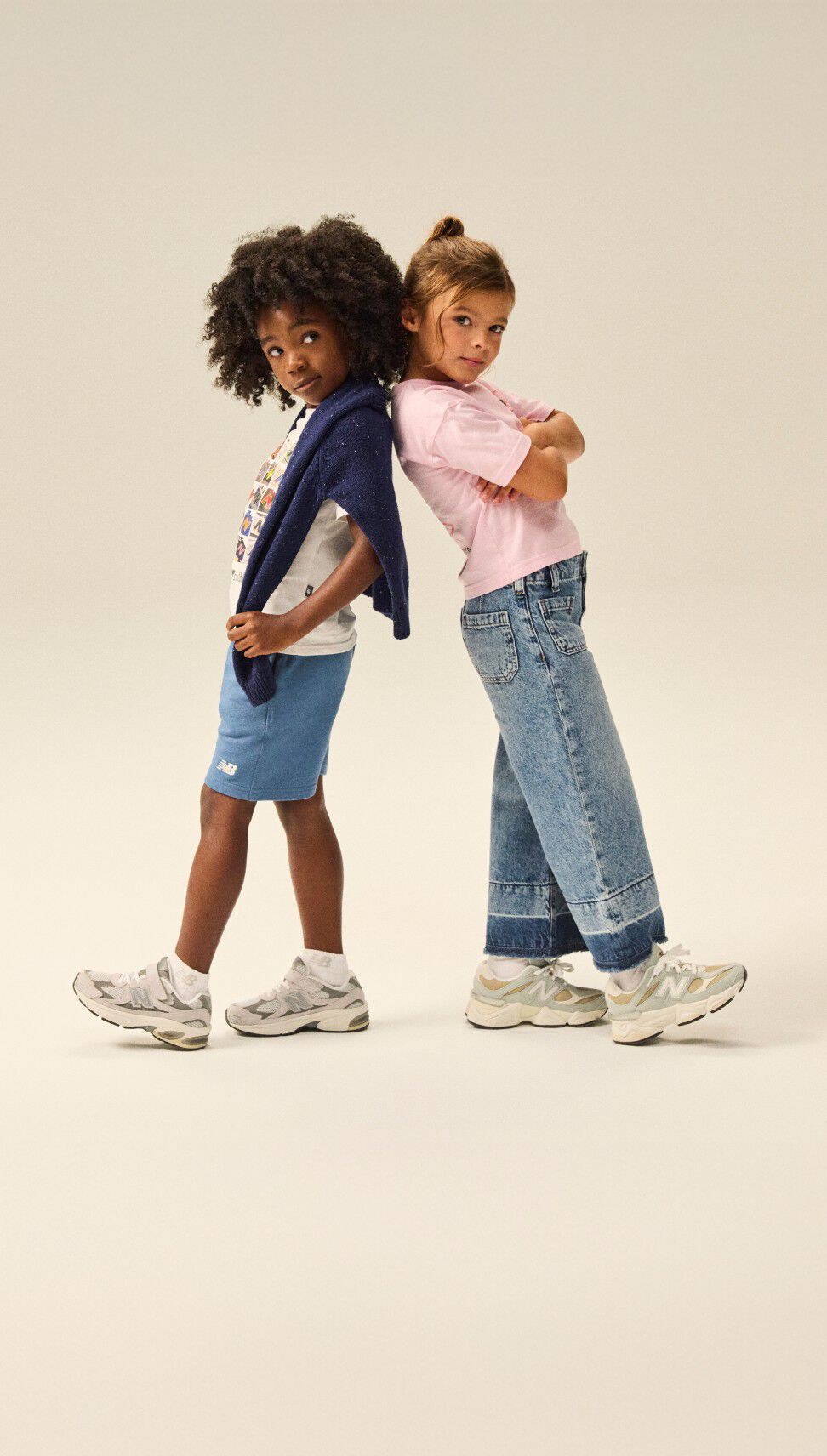 Two kids standing back to back wearing NB apparel and shoes 