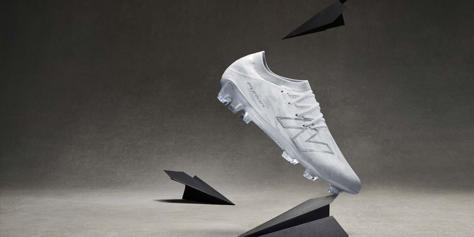 A bright yellow soccer cleat with black and red accents is displayed on its side among several glass prisms on a neutral gray surface. 