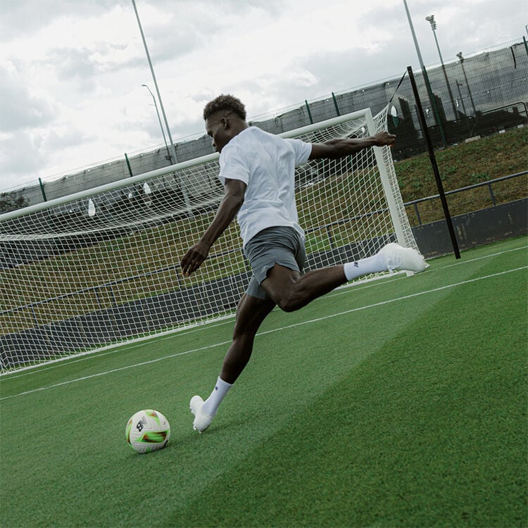 bukayo saka kicking a football ball to an emty goal with new balance football boots