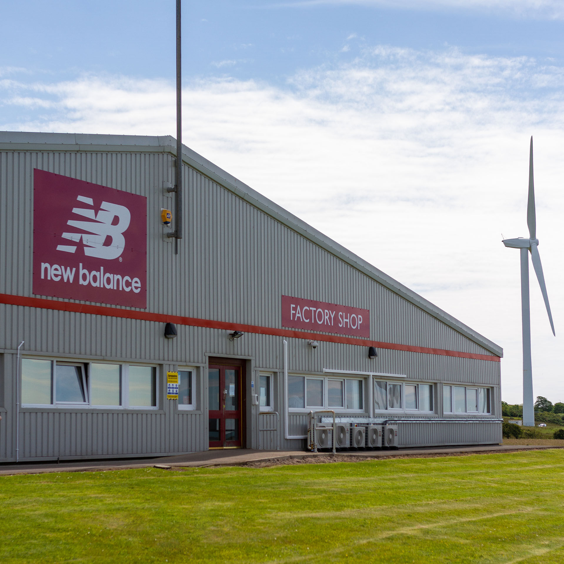Front exterior of factory shop surrounded by green grass, blue sky and windmill