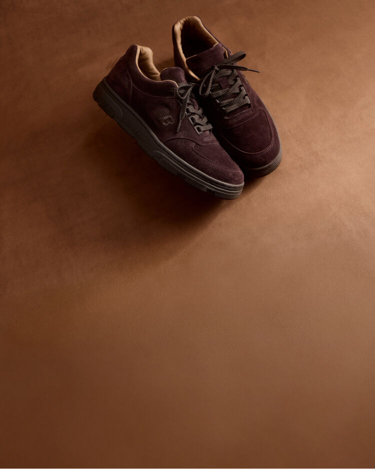 A pair of New Balance Made in UK sneakers in a brown textured studio environment. 