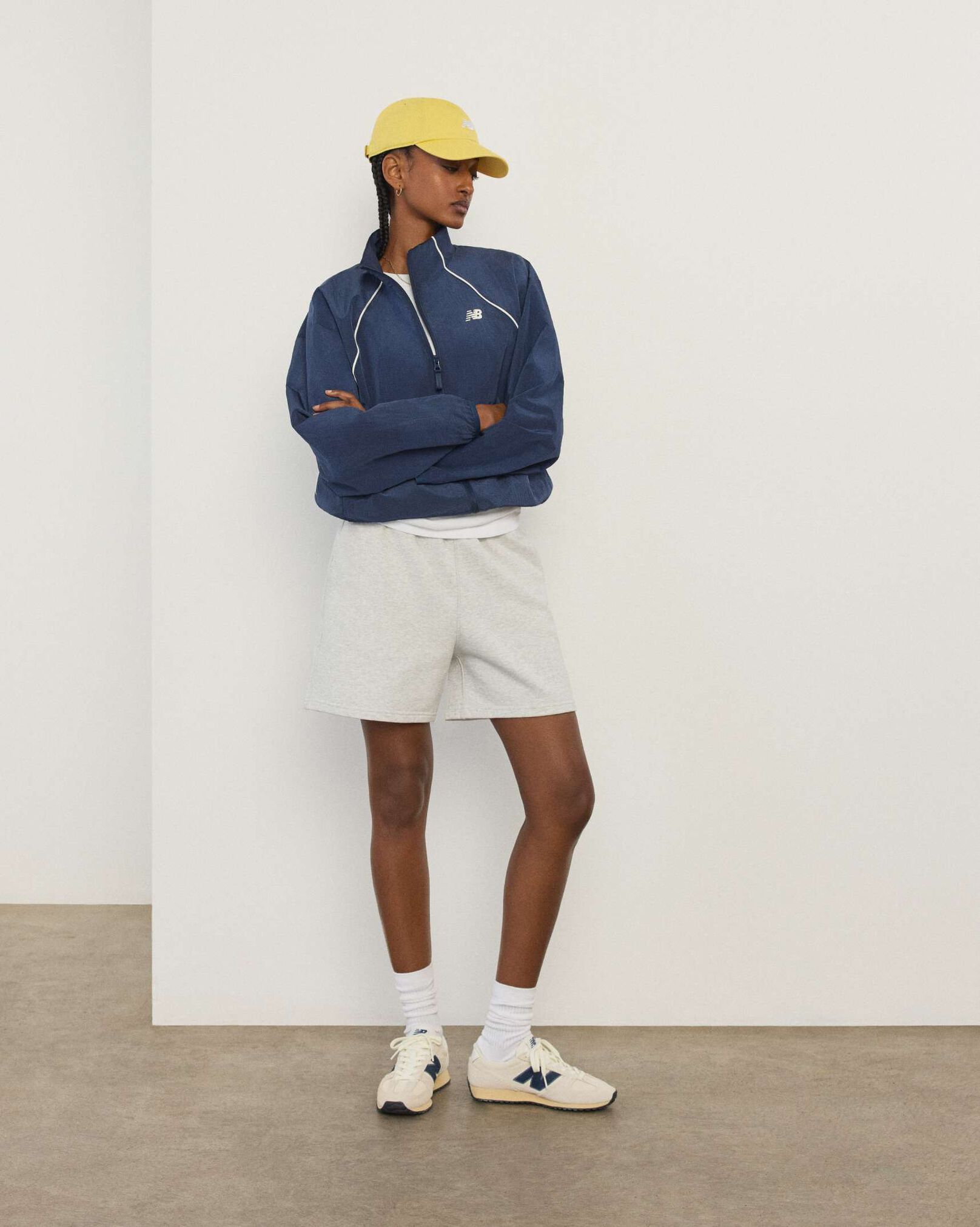 A woman wearing New Balance standing in front a white wall.