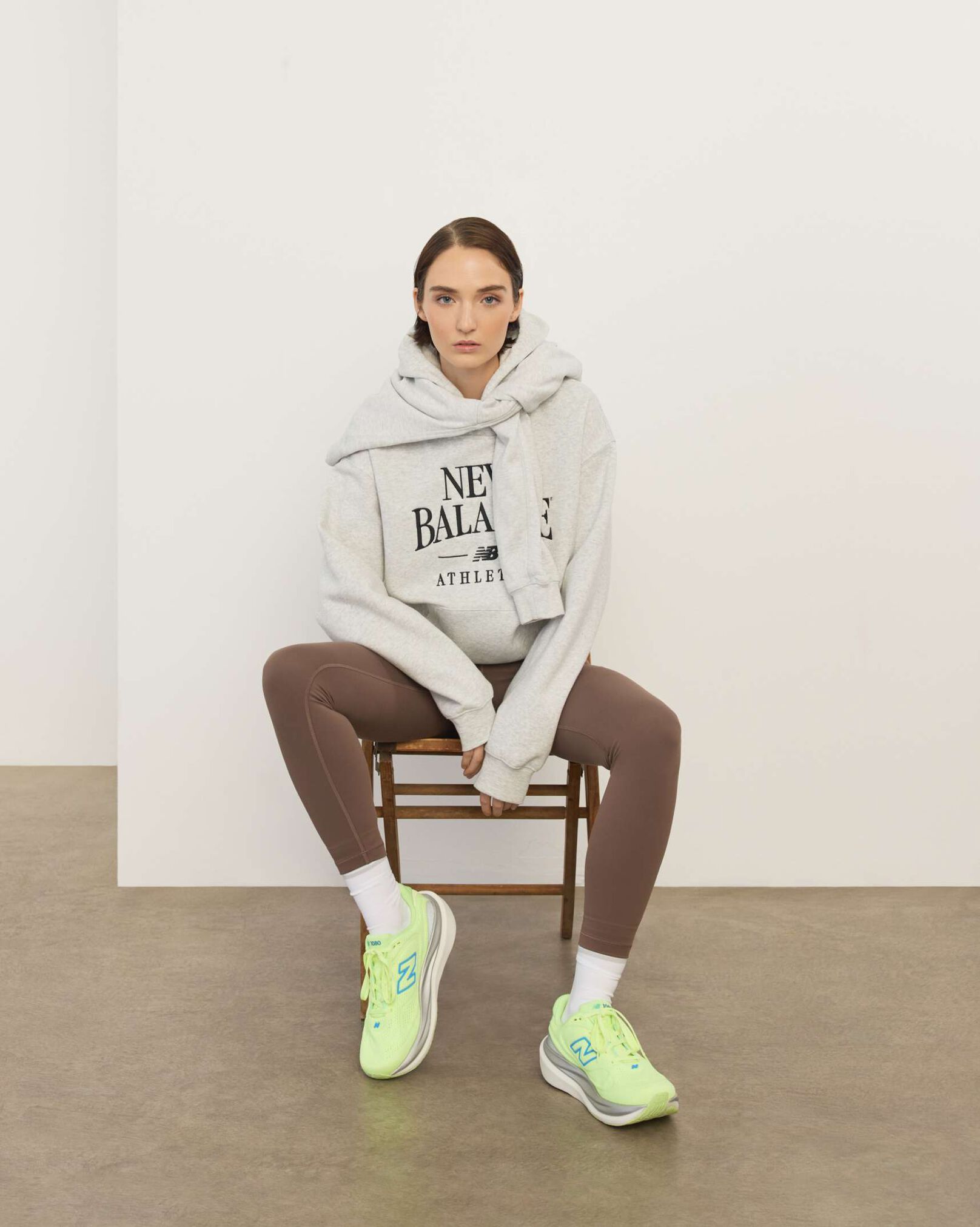 A woman wearing New Balance sitting in a chair in front a white wall.